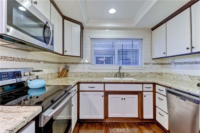 kitchen with appliances with stainless steel finishes, a raised ceiling, sink, and white cabinets