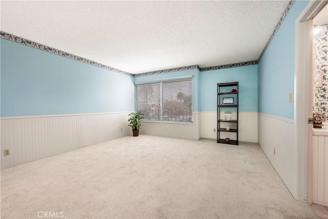 spare room with carpet floors, a textured ceiling, and wainscoting