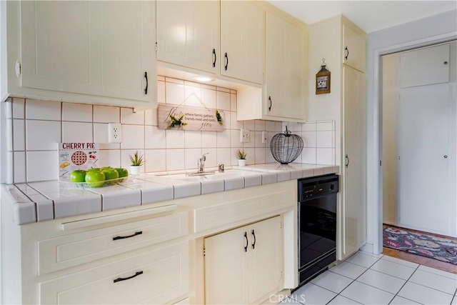 kitchen with black dishwasher, tile counters, tasteful backsplash, and a sink