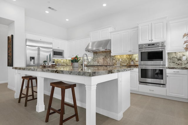 kitchen with a breakfast bar area, backsplash, built in appliances, and white cabinetry