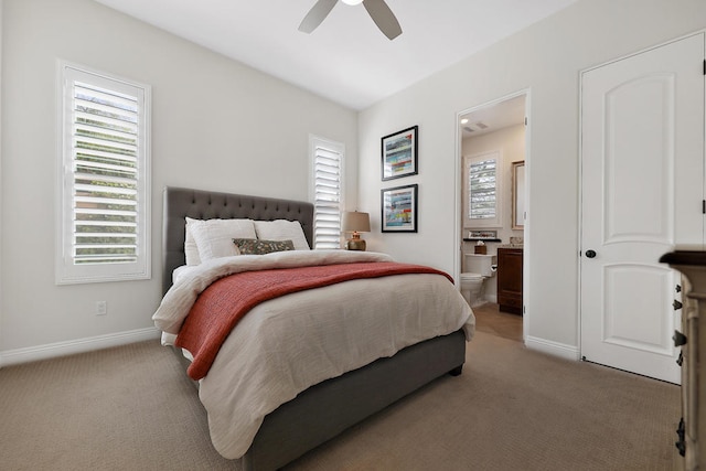 bedroom with connected bathroom, multiple windows, light colored carpet, and ceiling fan