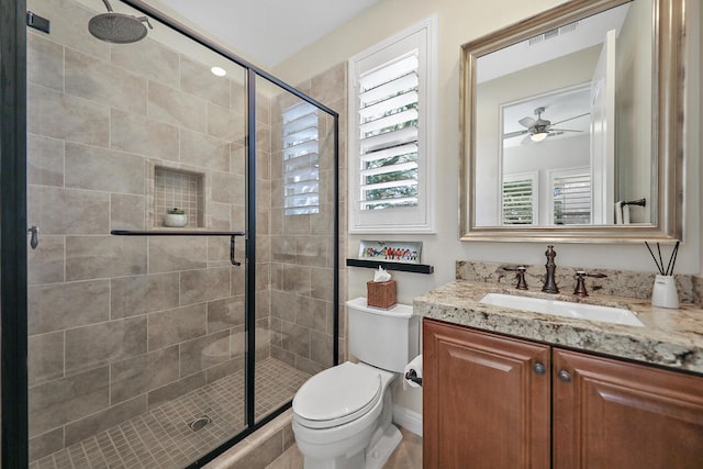 bathroom with vanity, a shower with shower door, toilet, and ceiling fan