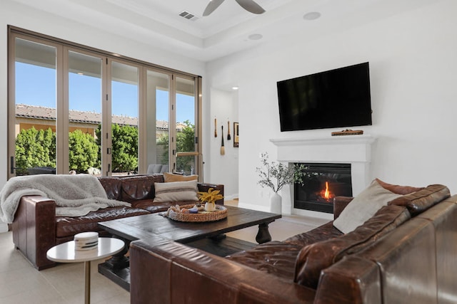 living room with light tile patterned floors, a raised ceiling, and ceiling fan