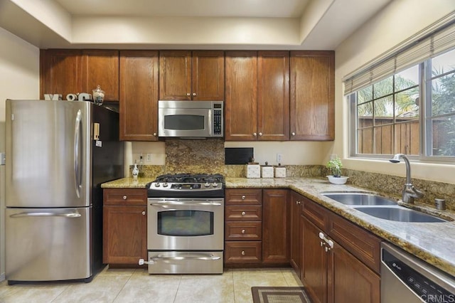 kitchen with light stone countertops, sink, a raised ceiling, light tile patterned floors, and appliances with stainless steel finishes