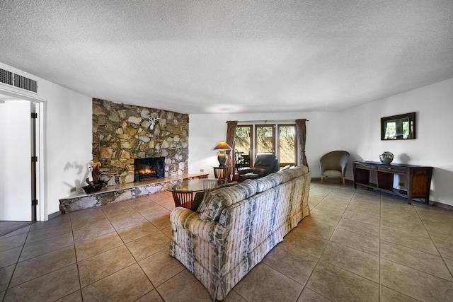 tiled living room with a stone fireplace and a textured ceiling