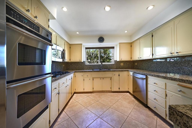 kitchen with decorative backsplash, sink, stainless steel appliances, and dark stone counters