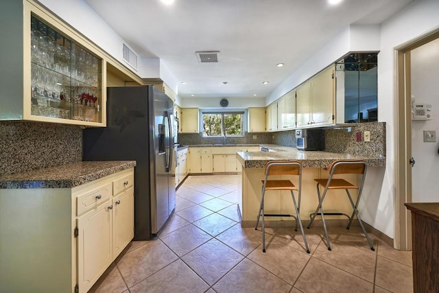 kitchen featuring a kitchen breakfast bar, decorative backsplash, stainless steel fridge, light tile patterned floors, and kitchen peninsula