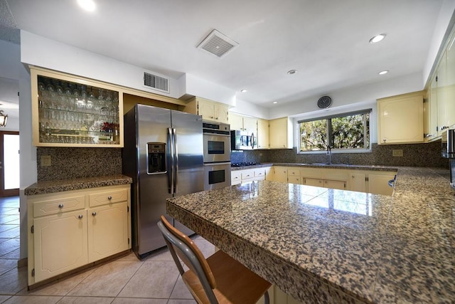 kitchen with appliances with stainless steel finishes, backsplash, sink, cream cabinets, and light tile patterned flooring