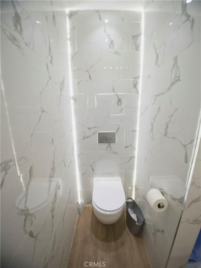 bathroom with toilet, stone wall, and wood finished floors