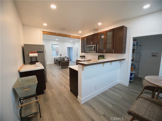 kitchen with a breakfast bar area, glass insert cabinets, stainless steel microwave, a peninsula, and light countertops