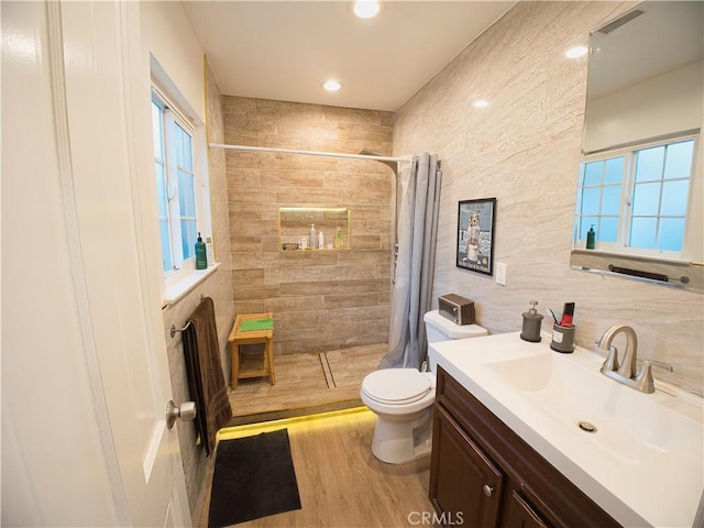 bathroom with visible vents, toilet, wood finished floors, a tile shower, and vanity