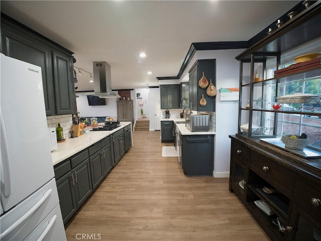 kitchen with light wood-style flooring, light countertops, freestanding refrigerator, tasteful backsplash, and island exhaust hood