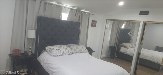 bedroom featuring dark wood finished floors, visible vents, vaulted ceiling, and two closets