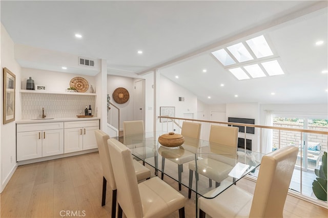 dining space with sink, lofted ceiling, and light wood-type flooring