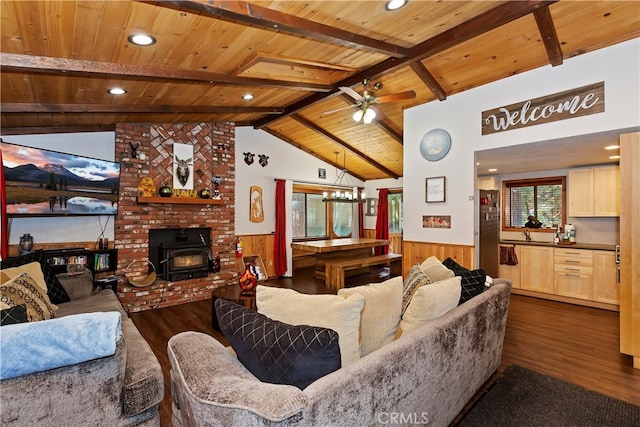 living room with vaulted ceiling with beams, a wood stove, dark hardwood / wood-style flooring, ceiling fan, and wood ceiling