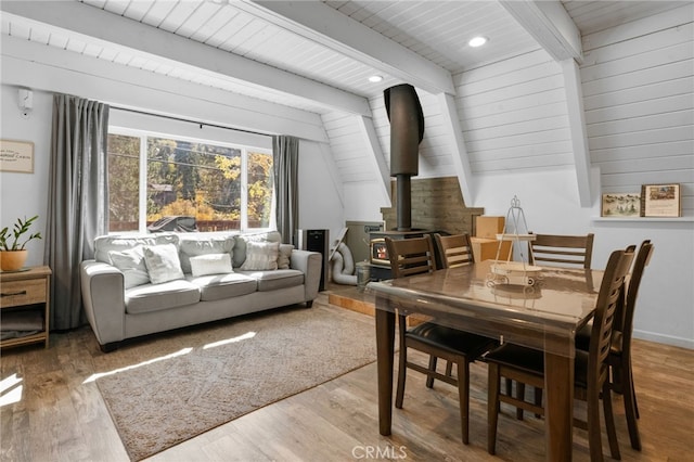 dining room featuring a wood stove, beam ceiling, hardwood / wood-style flooring, and wooden ceiling