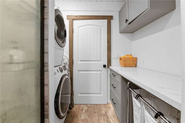 clothes washing area with light hardwood / wood-style flooring, stacked washing maching and dryer, and cabinets