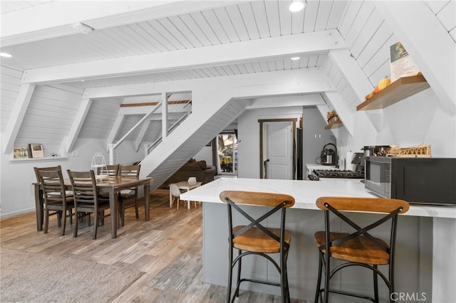 kitchen with light hardwood / wood-style flooring, a breakfast bar, vaulted ceiling with beams, and kitchen peninsula