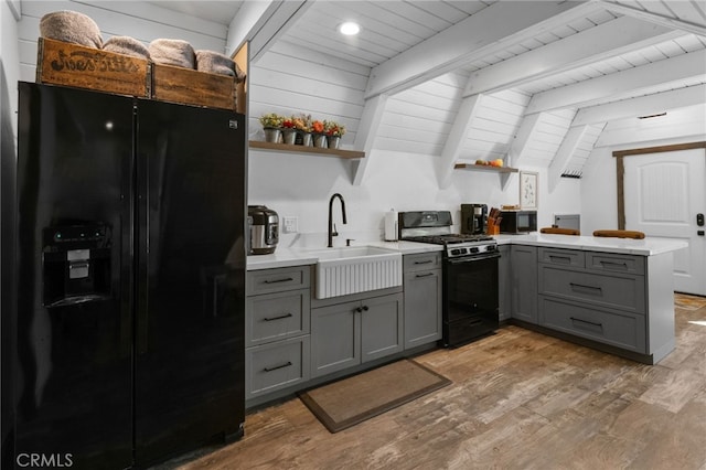 kitchen featuring hardwood / wood-style flooring, kitchen peninsula, sink, black appliances, and lofted ceiling with beams