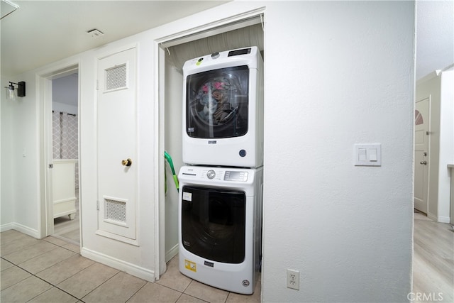 washroom with stacked washing maching and dryer and light tile patterned flooring