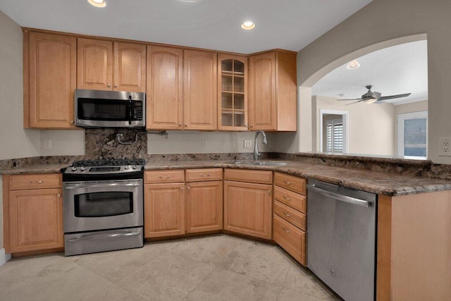 kitchen with ceiling fan, appliances with stainless steel finishes, sink, and dark stone counters