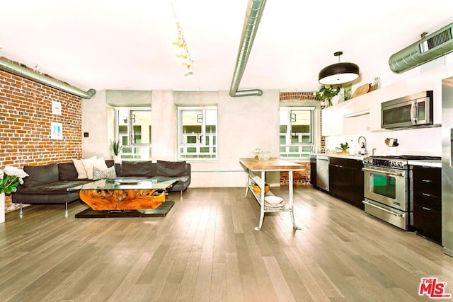 kitchen with appliances with stainless steel finishes, sink, hanging light fixtures, light hardwood / wood-style floors, and brick wall