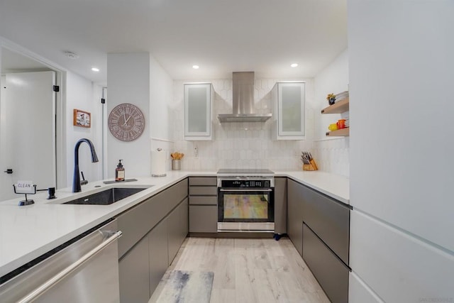 kitchen featuring wall chimney exhaust hood, stainless steel appliances, sink, gray cabinets, and light wood-type flooring