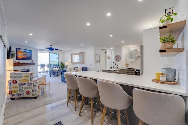 kitchen featuring kitchen peninsula, ceiling fan, a breakfast bar area, light hardwood / wood-style flooring, and sink