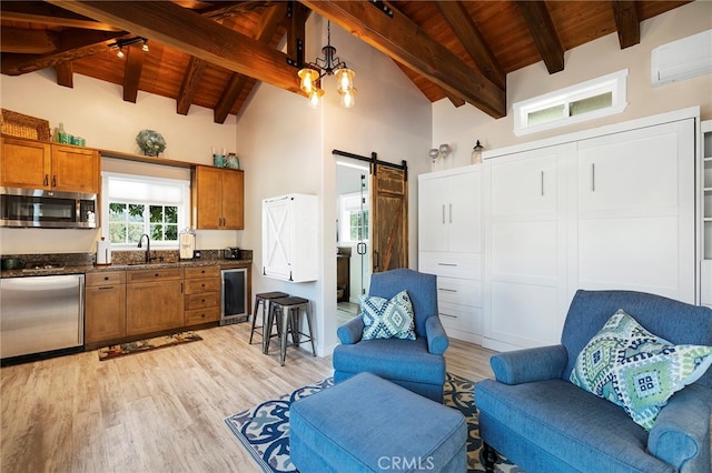 kitchen with beam ceiling, hanging light fixtures, appliances with stainless steel finishes, a barn door, and light hardwood / wood-style flooring