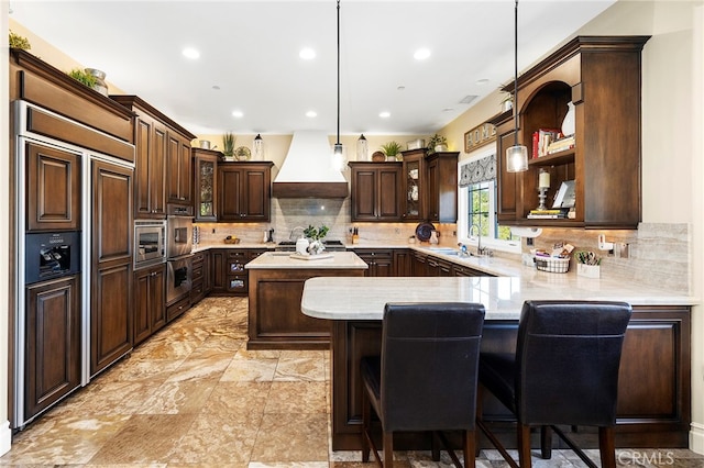 kitchen with hanging light fixtures, kitchen peninsula, stainless steel appliances, dark brown cabinetry, and custom exhaust hood