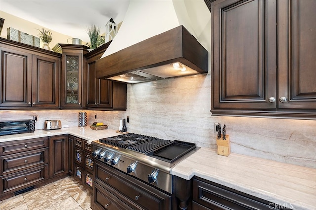 kitchen featuring custom exhaust hood, decorative backsplash, dark brown cabinets, stainless steel gas cooktop, and light stone counters