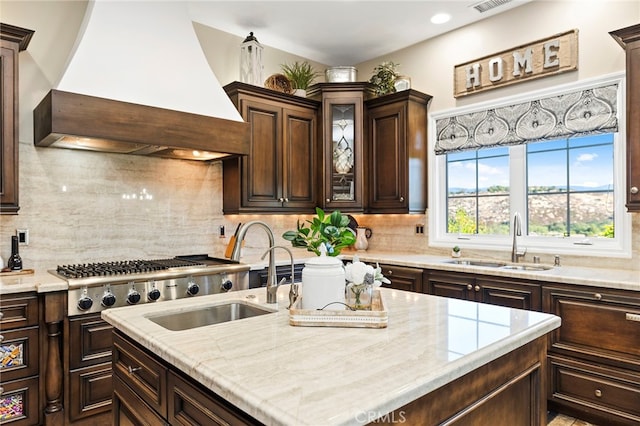 kitchen featuring custom exhaust hood, tasteful backsplash, stainless steel gas stovetop, dark brown cabinetry, and sink