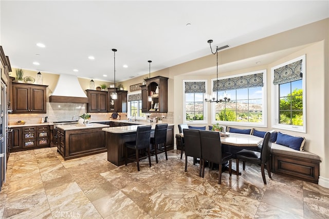 kitchen with custom range hood, decorative light fixtures, and plenty of natural light