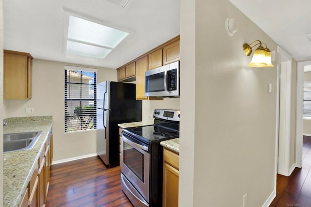 kitchen with appliances with stainless steel finishes, light stone countertops, dark hardwood / wood-style floors, a skylight, and sink