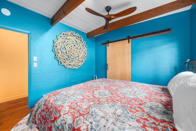 bedroom featuring beamed ceiling, dark wood-type flooring, a barn door, and ceiling fan