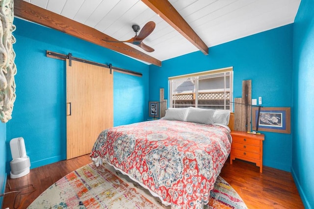 bedroom with ceiling fan, wood-type flooring, beamed ceiling, and a barn door