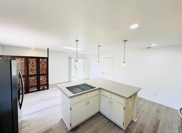 kitchen with black electric cooktop, stainless steel fridge, a center island, decorative light fixtures, and light wood-type flooring