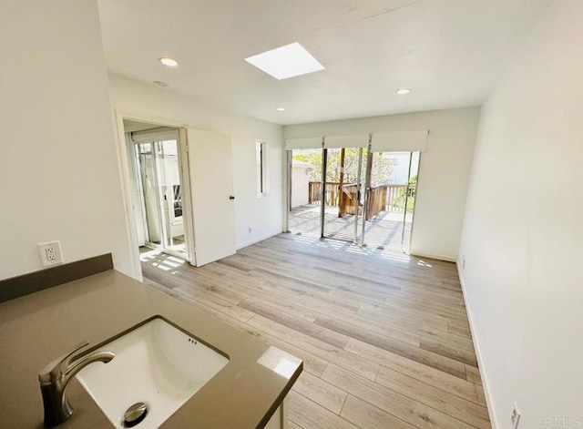 unfurnished room featuring light hardwood / wood-style flooring, sink, and a skylight