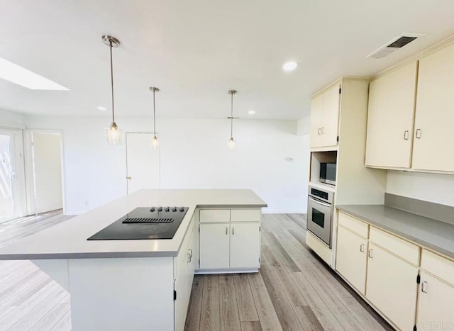 kitchen featuring appliances with stainless steel finishes, a kitchen island, hanging light fixtures, and light hardwood / wood-style floors