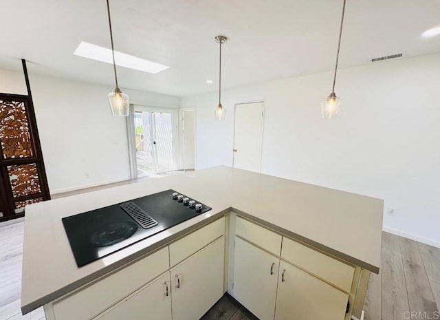 kitchen featuring black electric stovetop, light hardwood / wood-style floors, a skylight, and hanging light fixtures