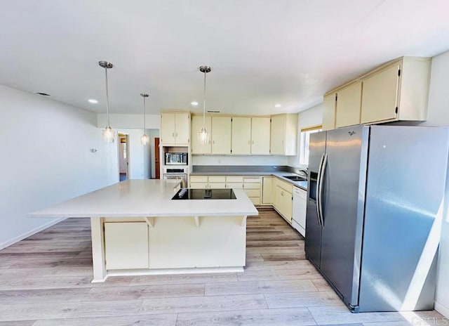 kitchen with cream cabinets, stainless steel appliances, a center island with sink, decorative light fixtures, and light hardwood / wood-style floors