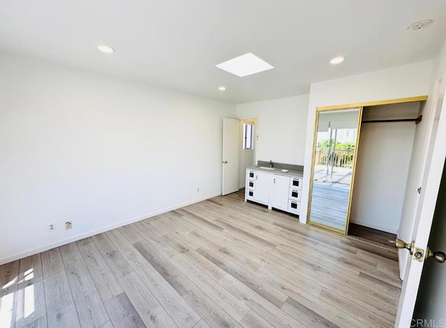 unfurnished bedroom featuring a closet, a skylight, sink, and light wood-type flooring