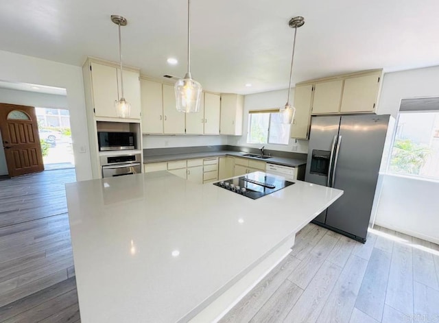 kitchen featuring cream cabinets, sink, pendant lighting, appliances with stainless steel finishes, and light hardwood / wood-style floors