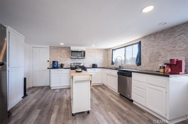 kitchen with appliances with stainless steel finishes, wood finished floors, a sink, white cabinetry, and backsplash