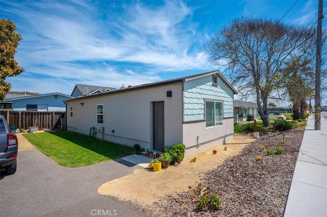 view of side of property featuring stucco siding, fence, and a yard