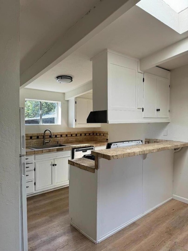 kitchen with kitchen peninsula, sink, light wood-type flooring, white cabinetry, and wall chimney range hood