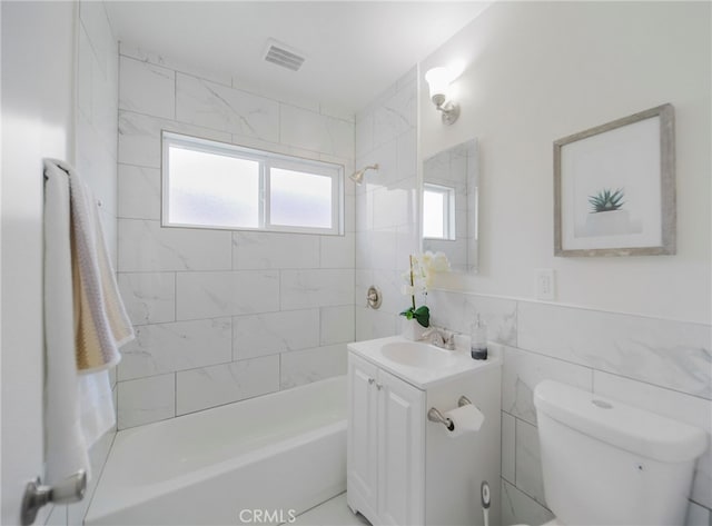 full bathroom featuring vanity, tiled shower / bath combo, toilet, and tile walls