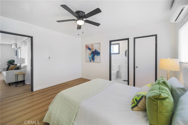 bedroom featuring connected bathroom, a wall mounted air conditioner, wood-type flooring, and ceiling fan