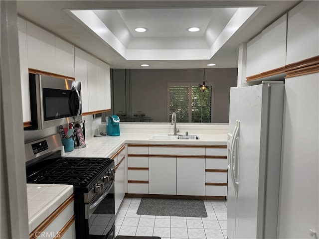 kitchen featuring light tile patterned flooring, sink, a tray ceiling, white cabinetry, and stainless steel appliances