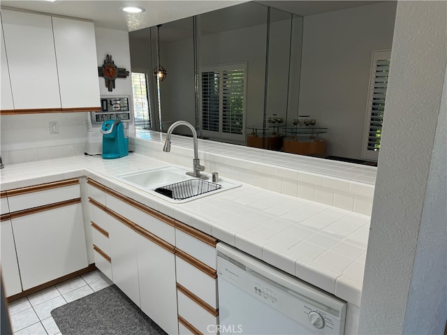 kitchen with white dishwasher, sink, tile counters, and white cabinets